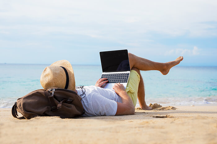 a person laying on the beach looking at a laptop which is powered off.