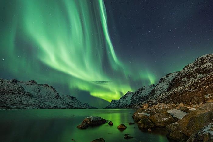 the northern lights accross a fjord, they are green and blue.