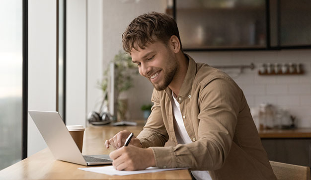 Young expat man working on a laptop at desk with pen in hand