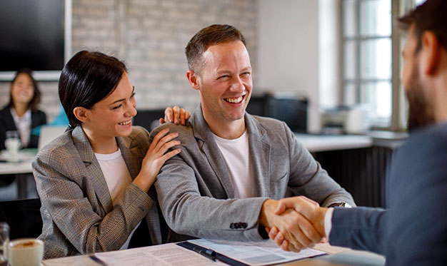 Financial adviser and client shaking hands and smiling across table