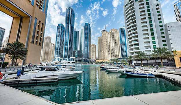 Looking up to Dubai skyscrapers and yachts in the marina on a bright day in the UAE