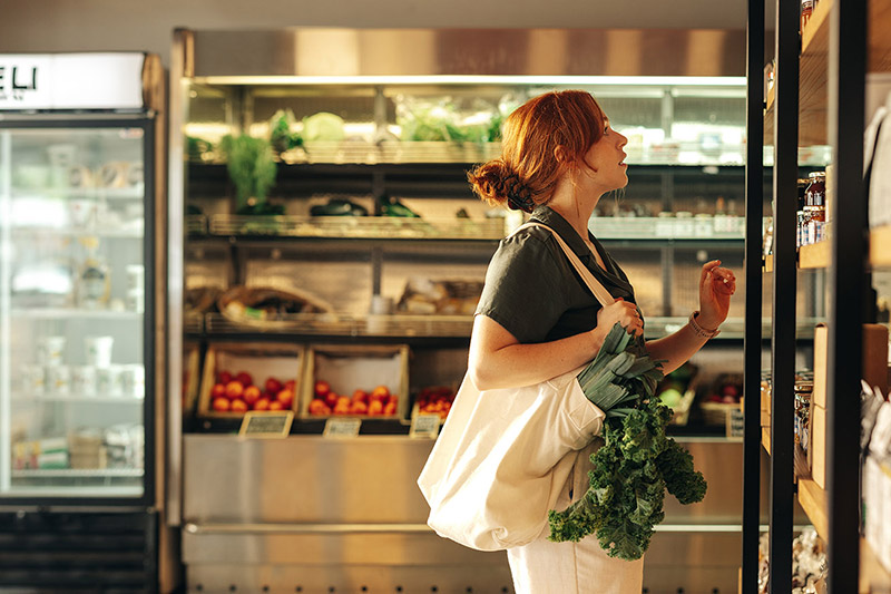 Side view of woman holding a tote bag and shopping for groceries