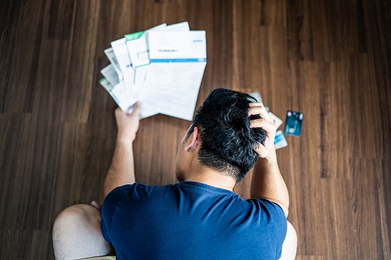 top back view of man ruffling his hair, looking at piles of paper