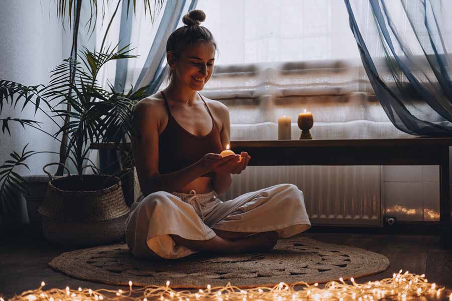 Smiling woman with a candle sitting cross legged on a mat