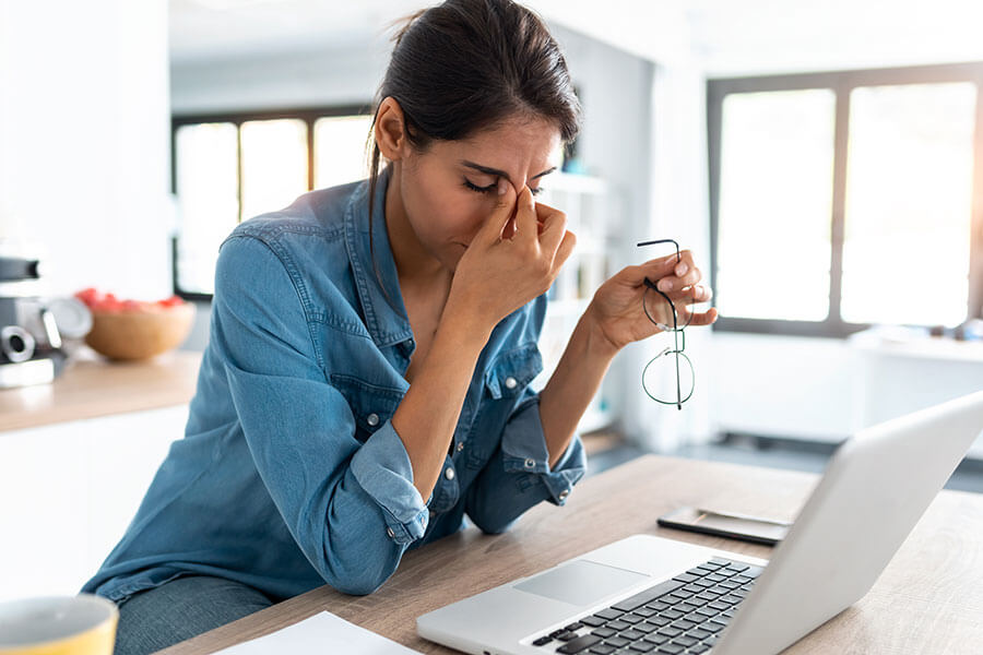 Woman massaging her forehead in front of a laptop