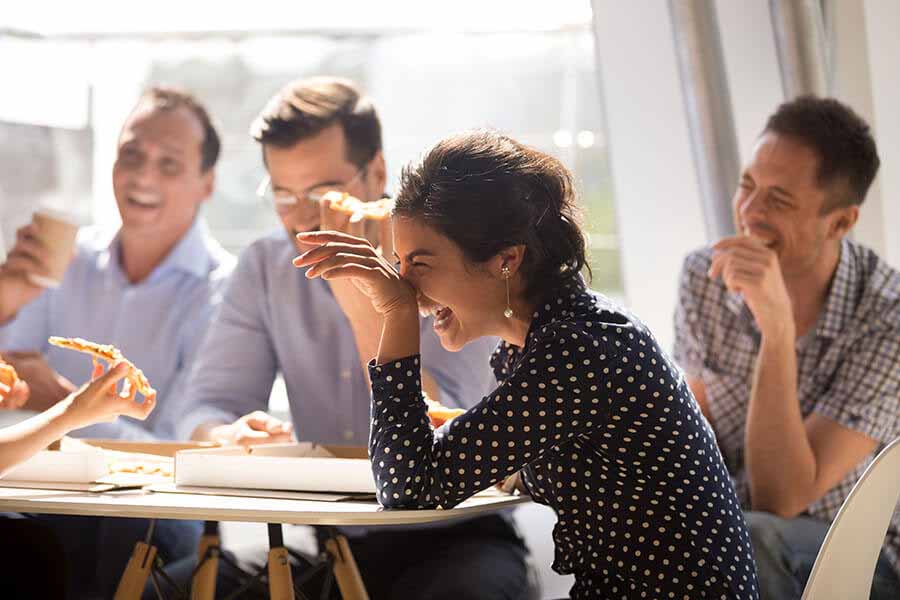 Group of people laughing together while eating pizza