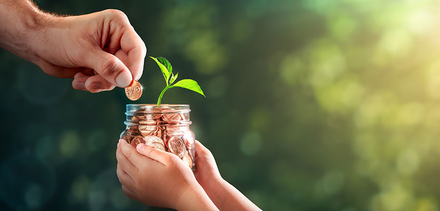 A plant growing out of a jar of pennies held in a child's hands while a man adds a coin