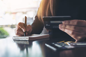 A woman making notes while holding a bank card