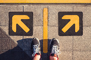 A bird's eye view of a pair of feet in front of two arrows on the ground pointing in different directions