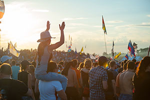 Coachella Festival- Woman on man’s shoulders, flags in the air, sunset over a festival