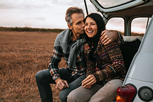 Couple sat in the boot of a car smiling and kissing