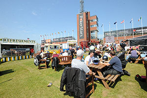 People sat on picnic benches with the grandstand and food vans behind