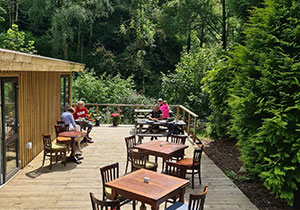People and tables on a deck outside the Lodge, surrounded by trees