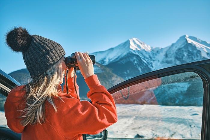 woman in a hat looking through a set of upside down binoculars and smiling.