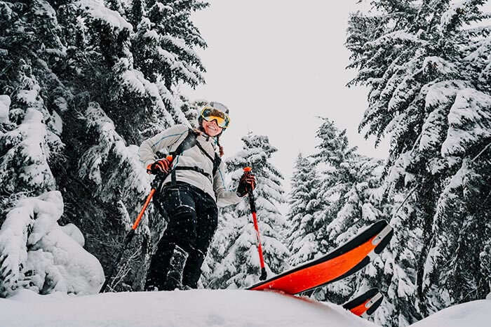 a smiling person with orange skis seen from below as if you fell over in the snow and are about to be run over.